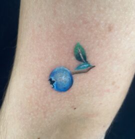A microrealism tattoo of a blueberry in full color performed by Basic Urban Witch Tattoo and Tarot in Fort Collins Colorado.