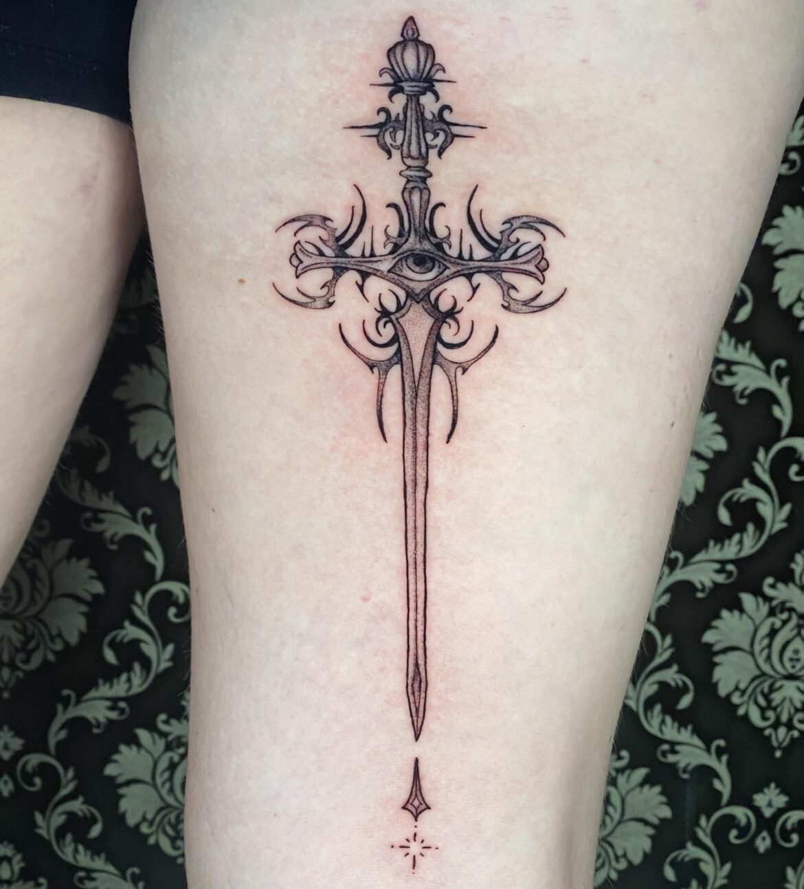 A fine line stippled tattoo featuring a sword with an eye performed by Basic Urban Witch Tattoo and Tarot in Fort Collins Colorado.